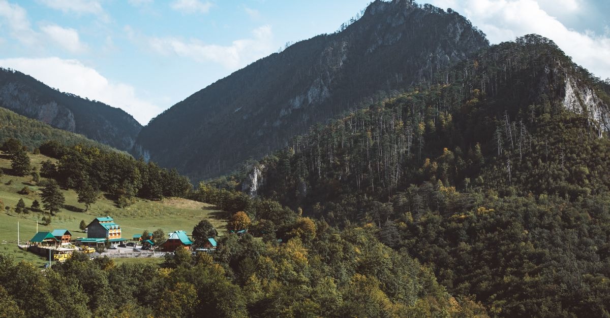 Charming mountain village nestled among lush green hills and dense forest with clear blue sky.