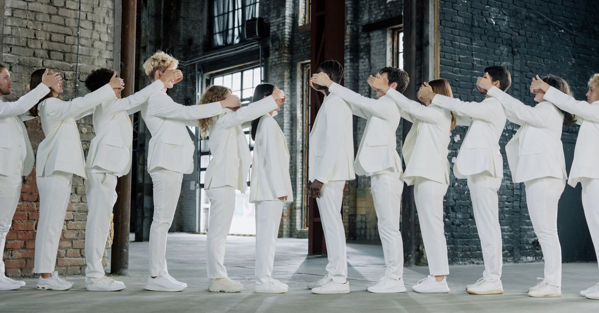 BTS boycotts 2027 Grammys over new Asian category Diverse group of adults in white suits standing in a line, covering each other's eyes in an industrial setting.