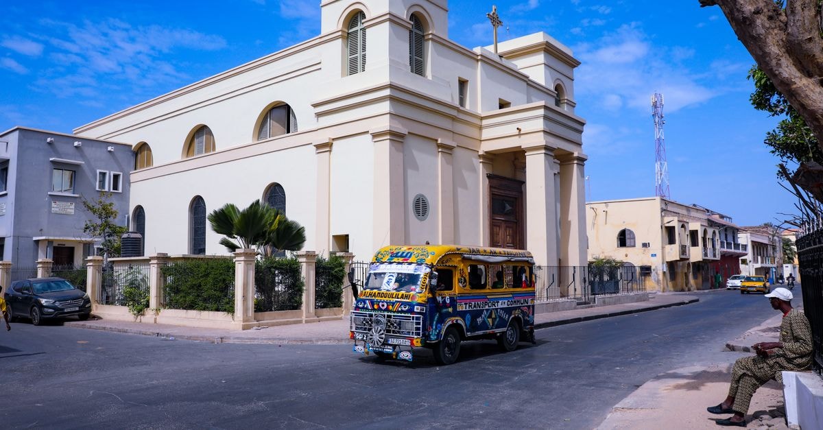 Moundou travel guide: timing, climate and getting around A vibrant minibus travels the streets of Dakar, passing a historic church under a clear blue sky.