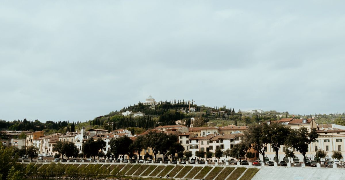 A picturesque Italian townscape featuring historic buildings and lush hills under a cloudy sky.