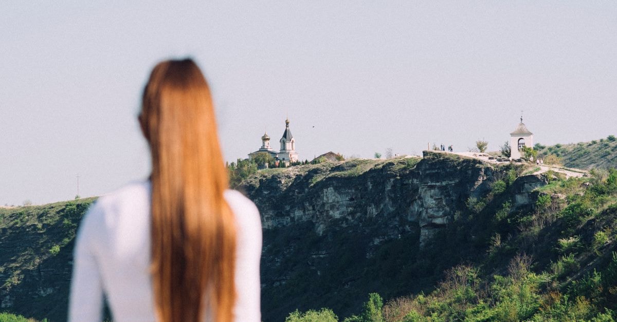 Glodeni travel guide: discovering Moldova's quiet northern heart Woman with long hair gazes at Orthodox church on cliff in Moldova.