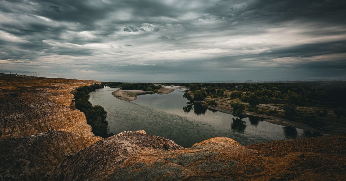 Dramatic landscape view of a winding river under a cloudy sky in Xinjiang, China.