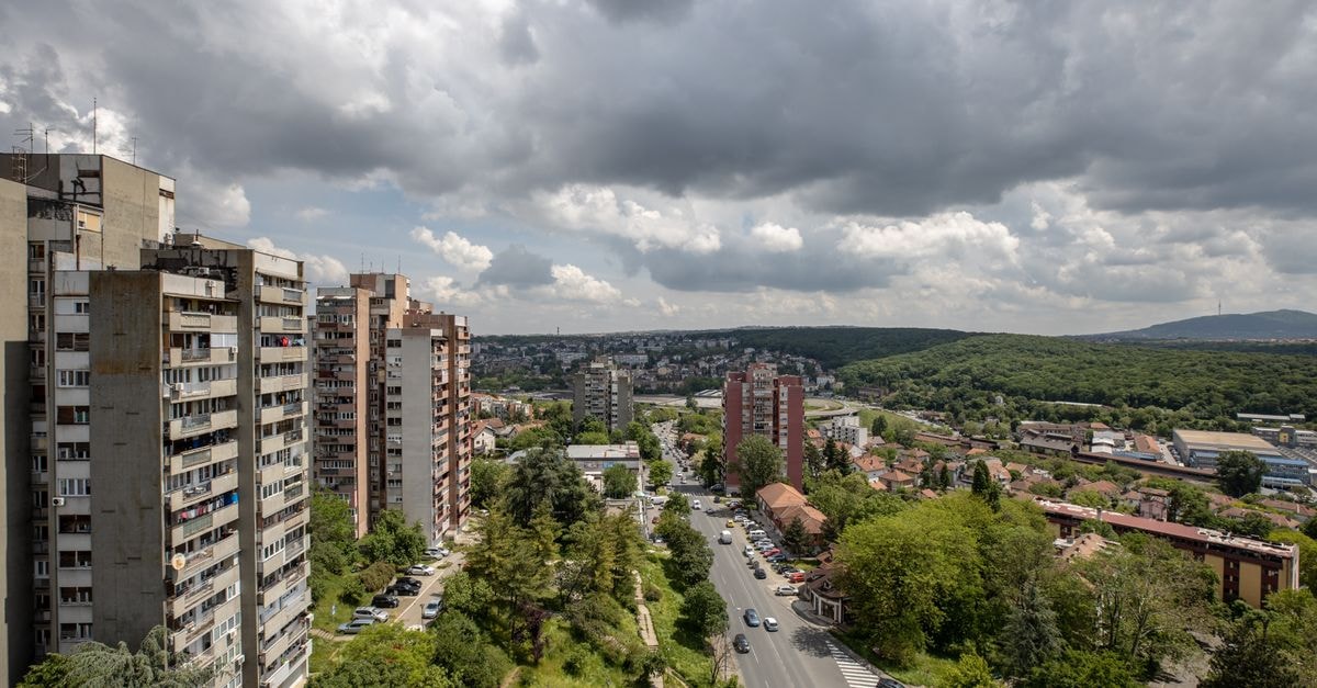 Aerial view of a cityscape featuring residential buildings, roads, and greenery under a cloudy sky.