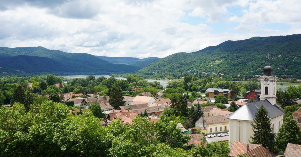 A picturesque aerial view of Visegrád, Hungary featuring a church, rooftops, and lush mountains.