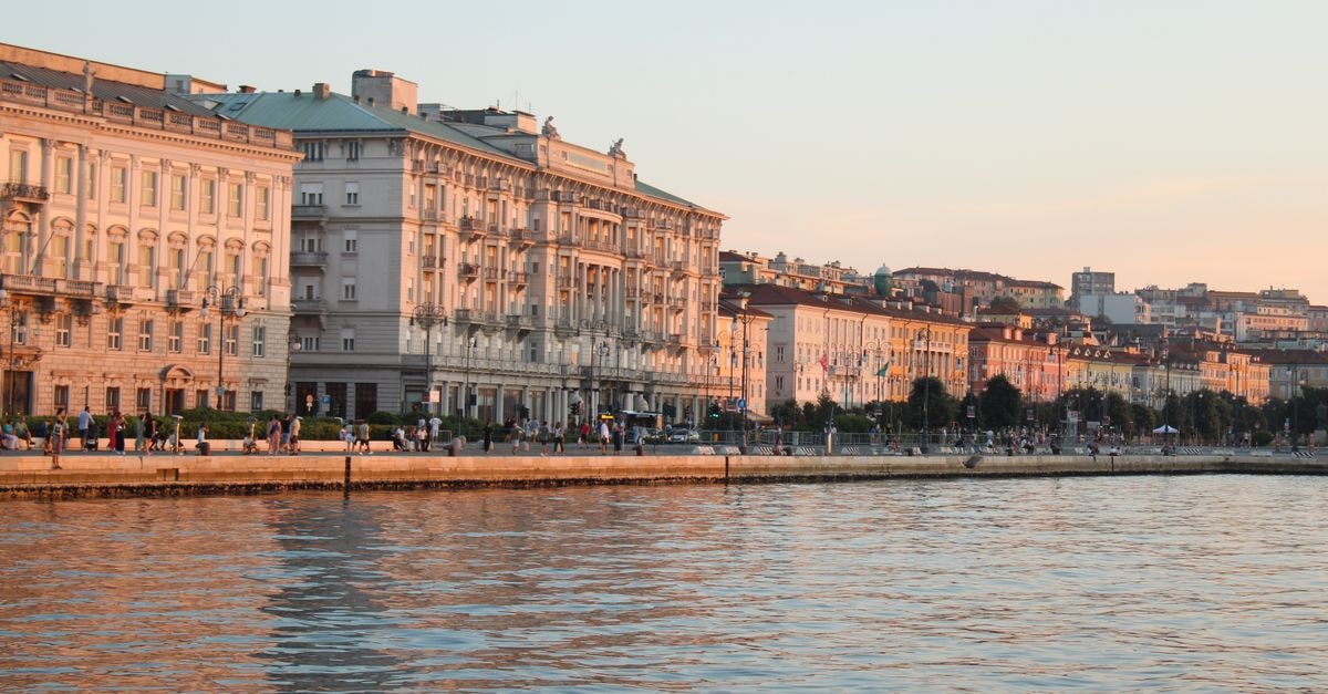 Beautiful sunset over historic waterfront buildings in Trieste, Italy reflecting off the Adriatic Sea.