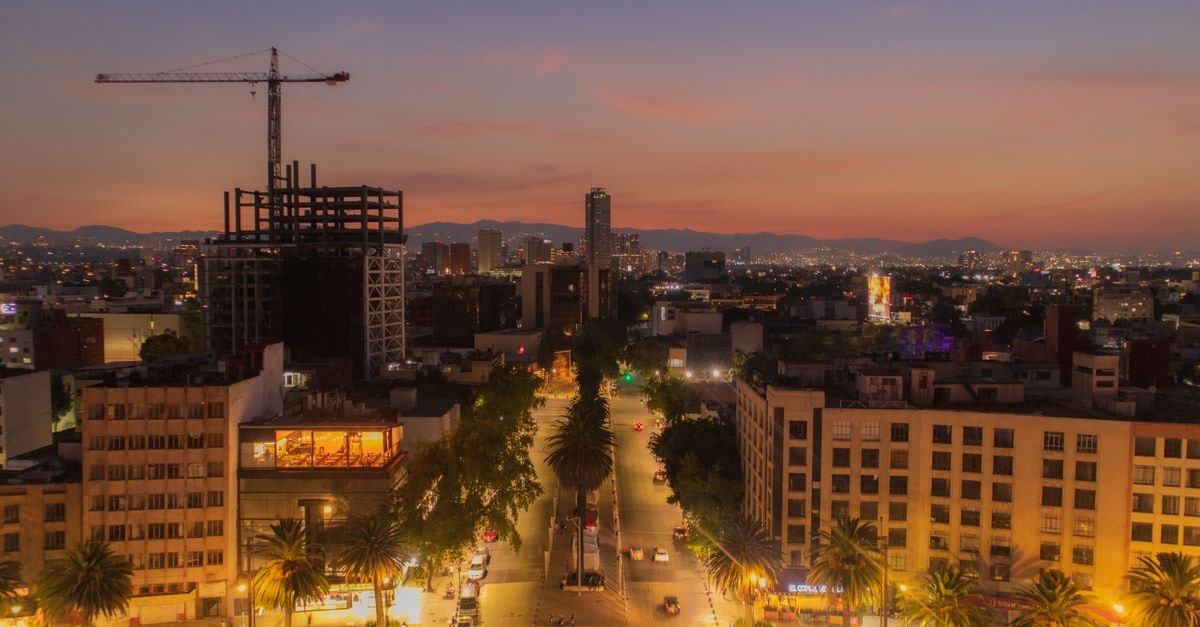 Aerial view of Mexico City's illuminated skyline at twilight, showcasing urban life and architecture.