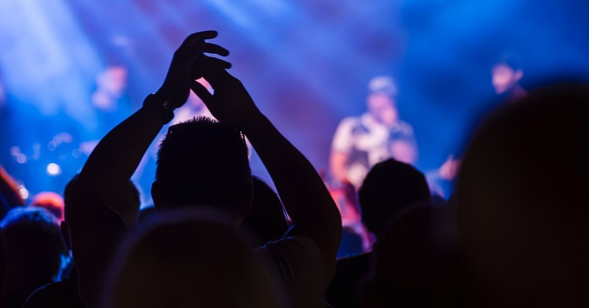 Energetic crowd at a live music concert with vibrant lighting and clapping hands.