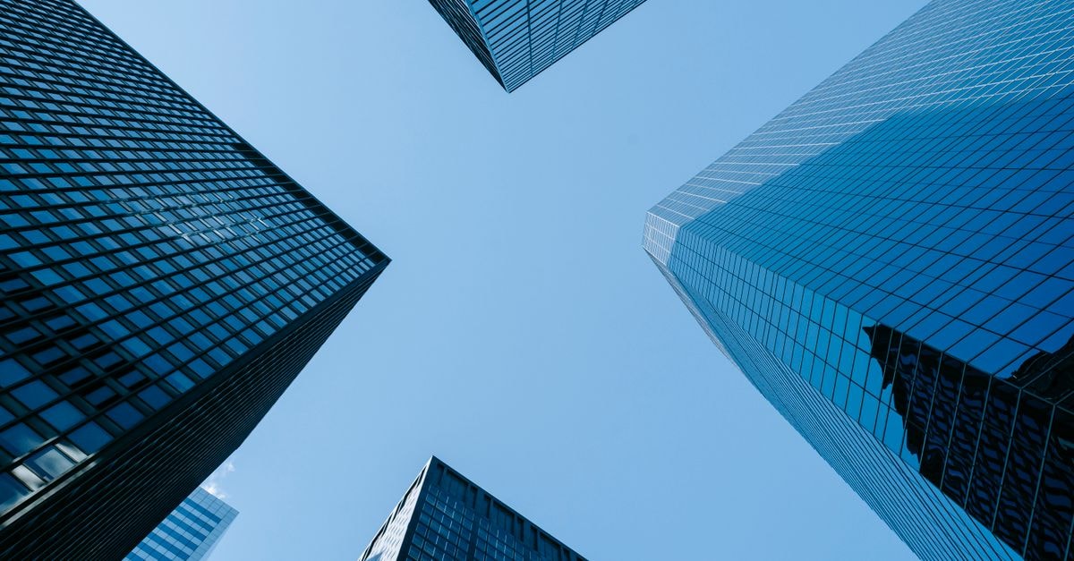 Low angle of high business towers with glass mirrored windows located in megalopolis downtown against blue sky