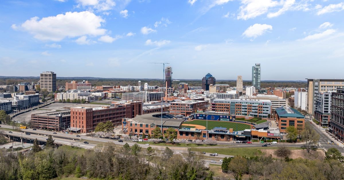 Greensboro Proximity 飯店:LEED 白金級棉紡廠再造之作 晴天空中俯瞰照片,展現 Durham 市中心充滿活力的天際線與城市景觀。
