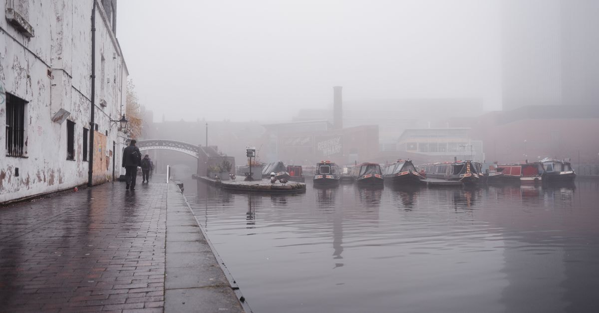 Birmingham Travel Guide: Weather Rhythm and Getting Around Many boats moored on calm water surface near paved waterfront with people walking near shabby building in town on foggy weather