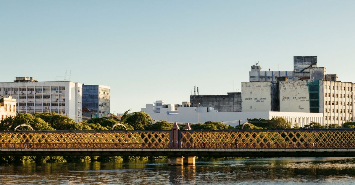 Serene view of a heritage bridge and urban skyline reflecting in calm waters during the day.
