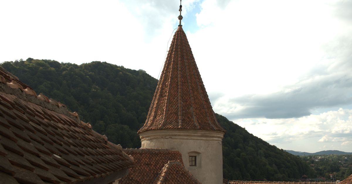 View of Bran Castle's iconic tower with surrounding lush hills under a bright sky in Romania.