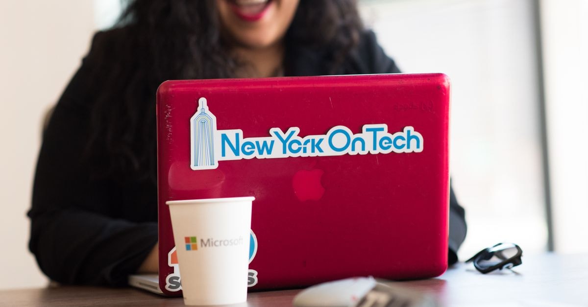 Microsoft Fiscal 2027 First-Quarter Earnings Preview Young woman working remotely with a laptop in a modern indoor office setting, showcasing tech culture.