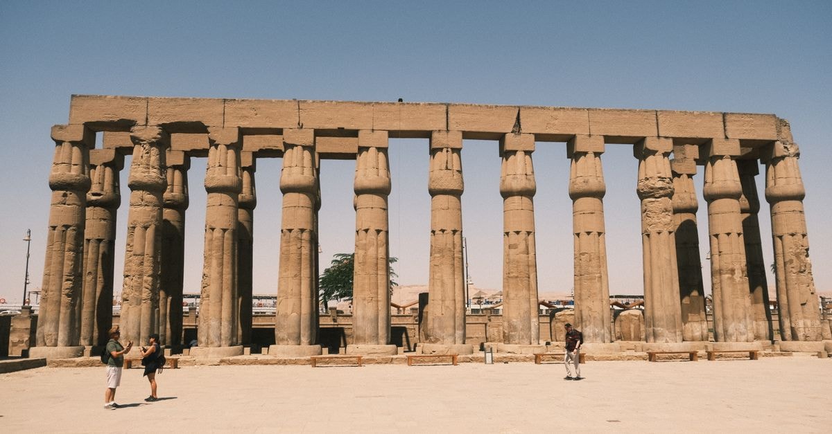 Ancient stone columns of Luxor Temple in Egypt with tourists visiting under a clear sky.