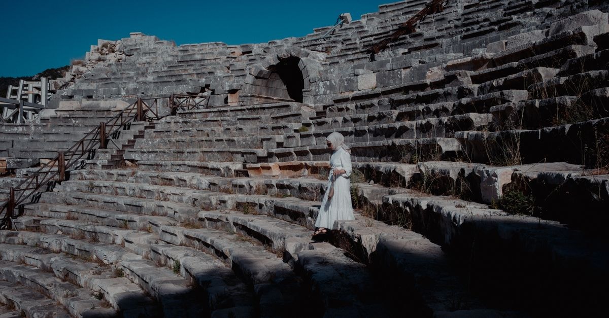 A woman in a white dress walks through the ancient theatre ruins in Kaş, Antalya.