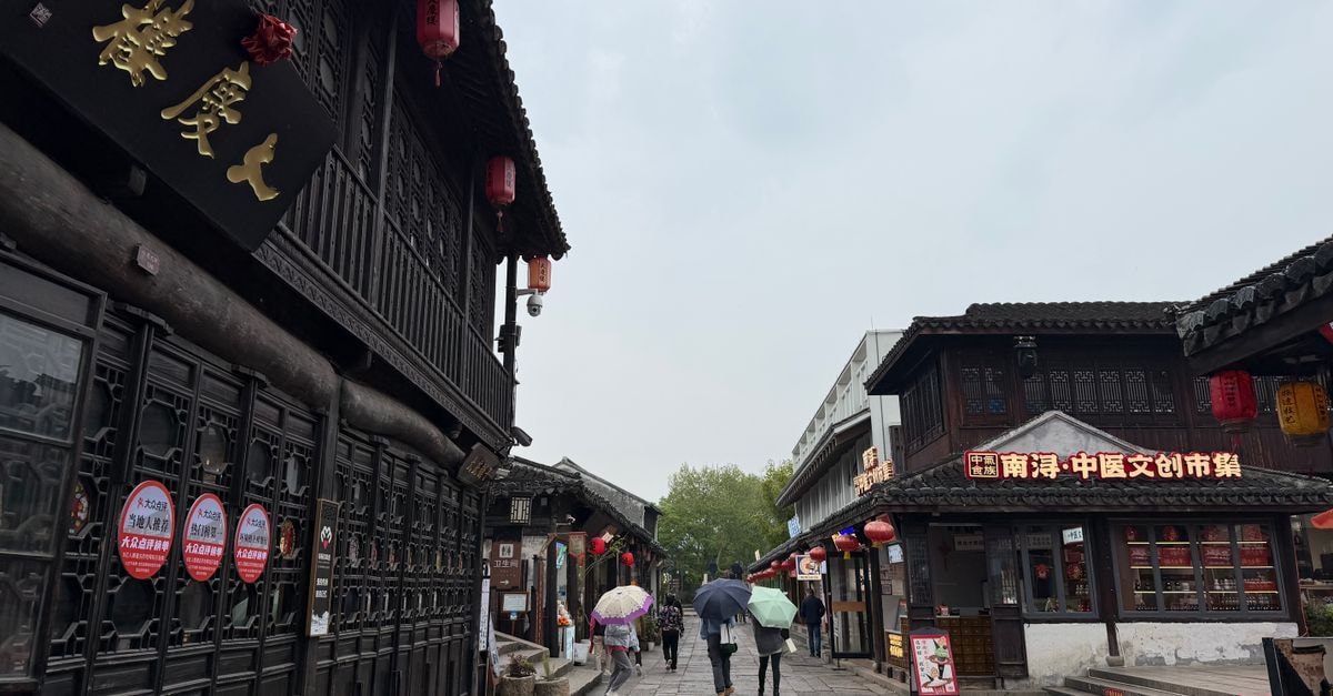 A rainy day in a historic Chinese street with people walking under umbrellas.