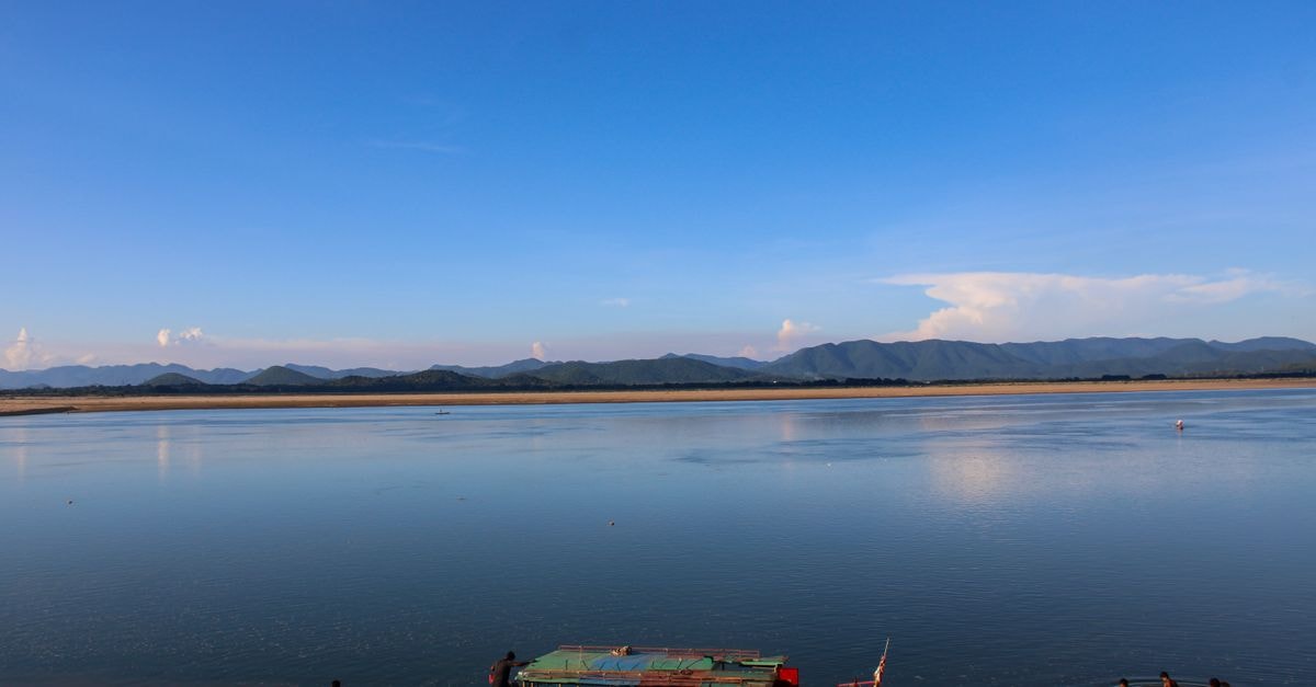 A calming river scene in India with distant mountains and a colorful boat.