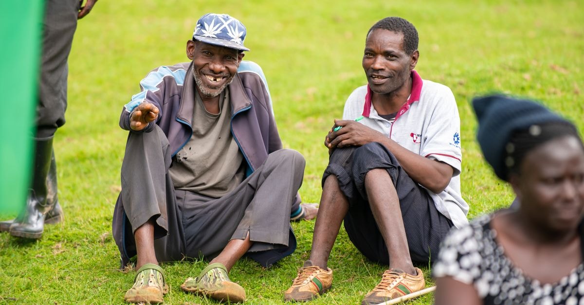 Eldoret State Lodge, Eldoret: A Presidential Residence in Uasin Gishu County Two men sitting happily on grass in Eldoret, Kenya, enjoying a sunny day outdoors.