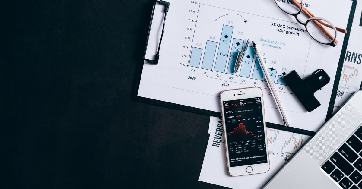 Top view of financial reports, smartphone showing stock market data, and a laptop on desk.