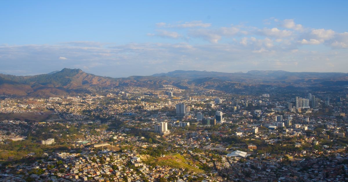 Aerial view of Tegucigalpa city with mountain backdrop under a clear blue sky.
