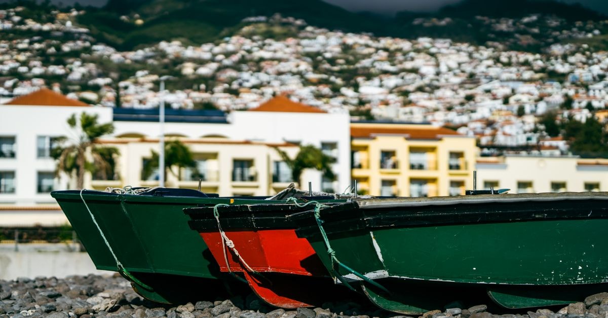 Sirius in Funchal: Rooftop Terrace Over the Old Town Vibrant fishing boats rest on the rocky shores of Madera with a coastal townscape in the background.