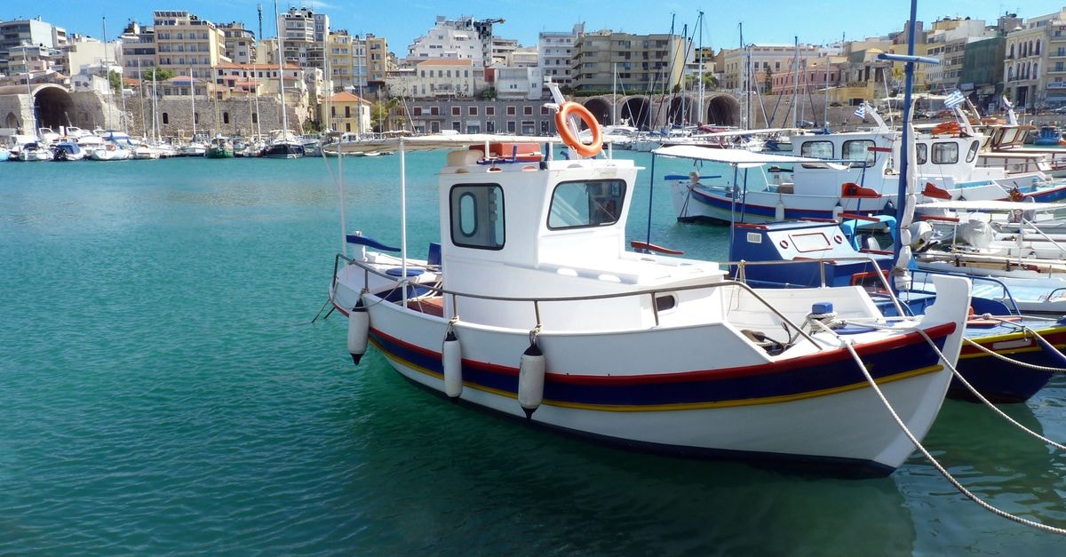 Heraklion Travel Guide: Planning Tips, Costs and Things to Do Modern white boats moored on turquoise water in harbor in sunny day with coastal city in distance against cloudy sky