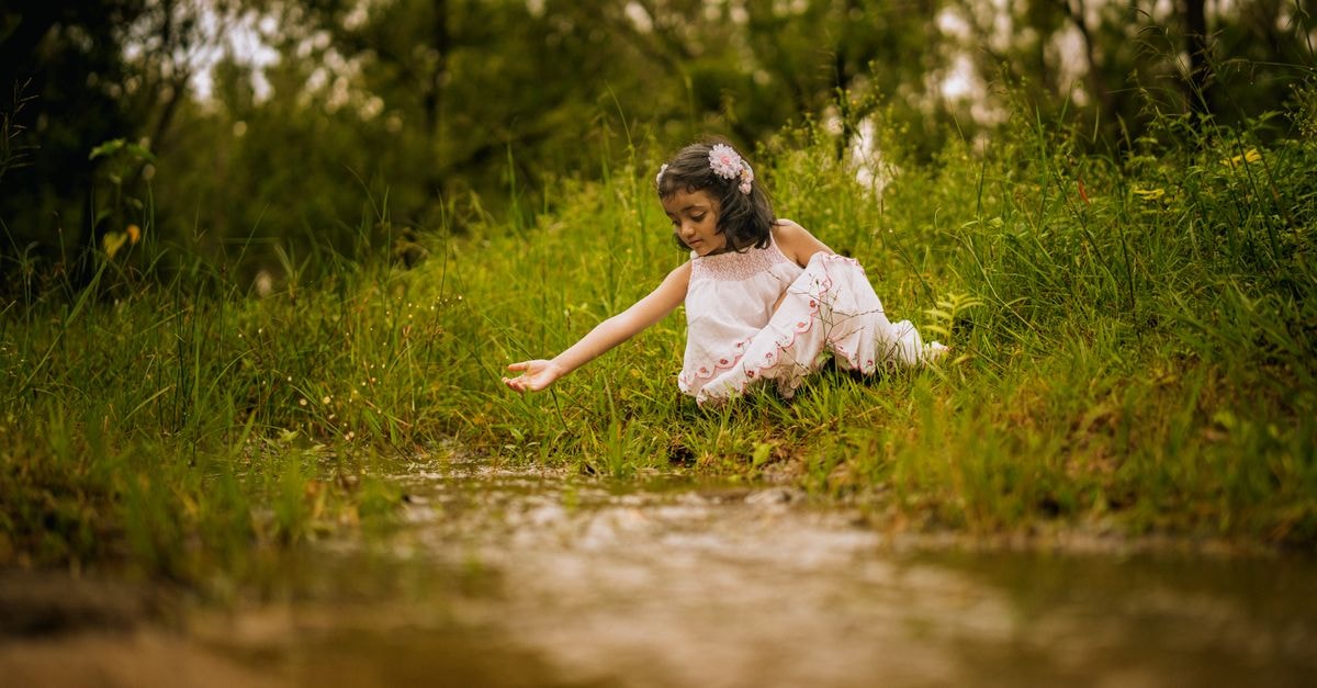 A young girl in white dress exploring the riverside in lush greenery during summer in Tumakuru, India.