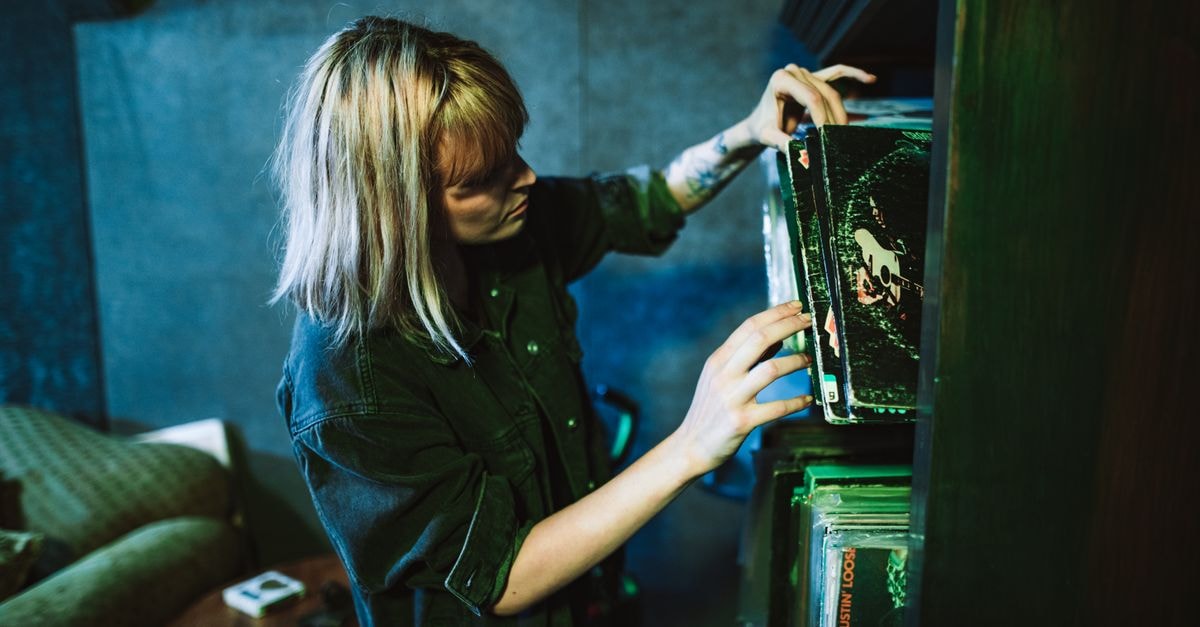 Sam Fender and Olivia Dean's "Rein Me In" sets longest-running UK No. 1 record A woman in a music studio choosing vinyl records from a shelf.