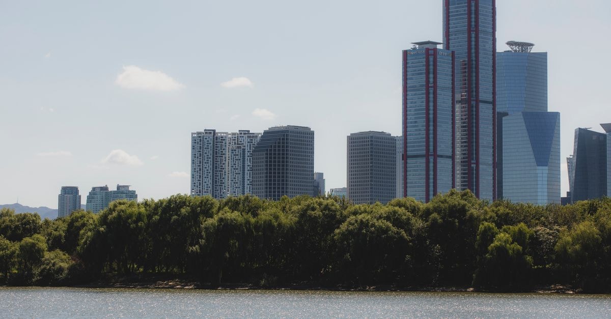 James Joyce Coffetel Mudanjiang: A Coffee-Themed Stay Near the Station Pedestrian Street Cityscape featuring a modern skyline with tall reflective skyscrapers and a riverbank.