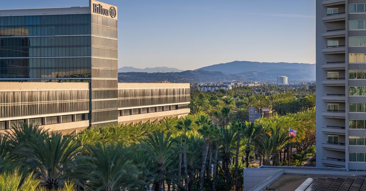 View of Hilton hotel surrounded by palm trees with mountains in the background at sunrise.