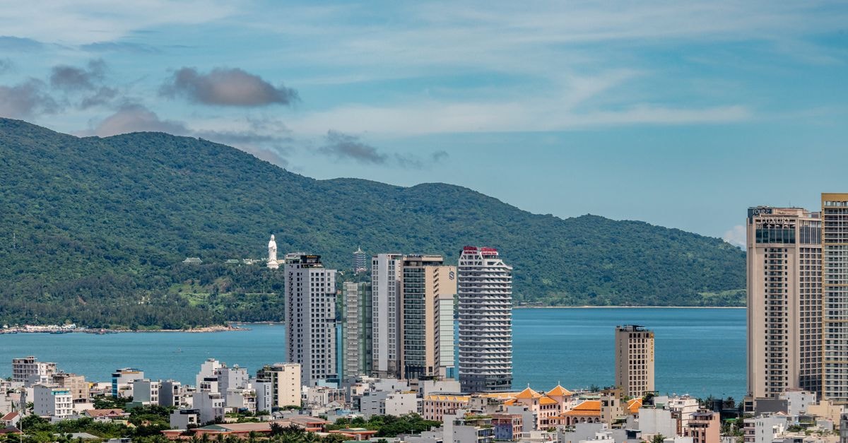 Cityscape of Da Nang, Vietnam with buildings, ocean, and lush mountains.