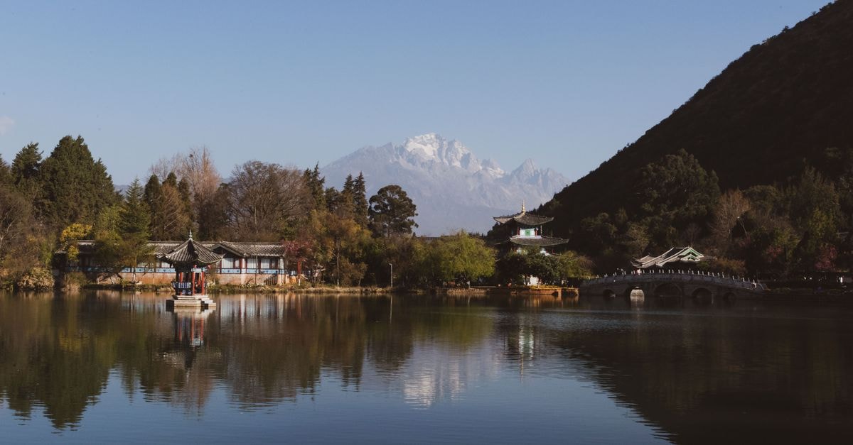 A Quiet Baoshan Travel Guide for Curious Yunnan Travelers A tranquil lakeside view with traditional architecture and mountains in the background.