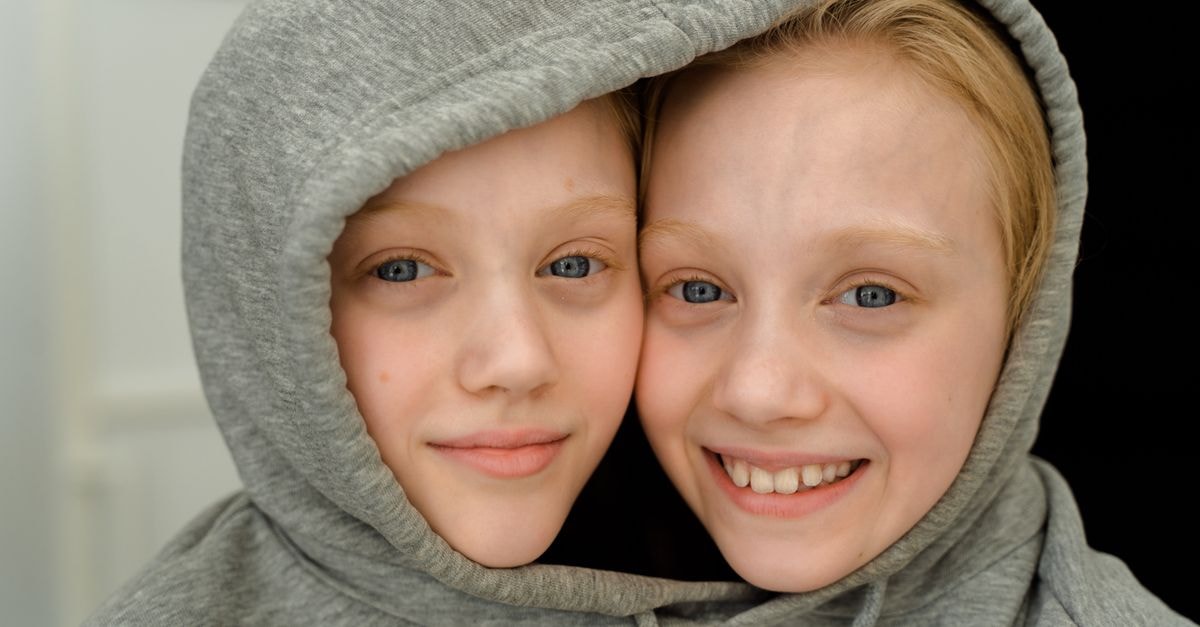 Recent Daily Show episodes feature Twin Temple debut, Kaitlan Collins interview and Klepper's Trump memorial breakdown Charming close-up of smiling twin girls with blonde hair sharing a grey hoodie indoors.