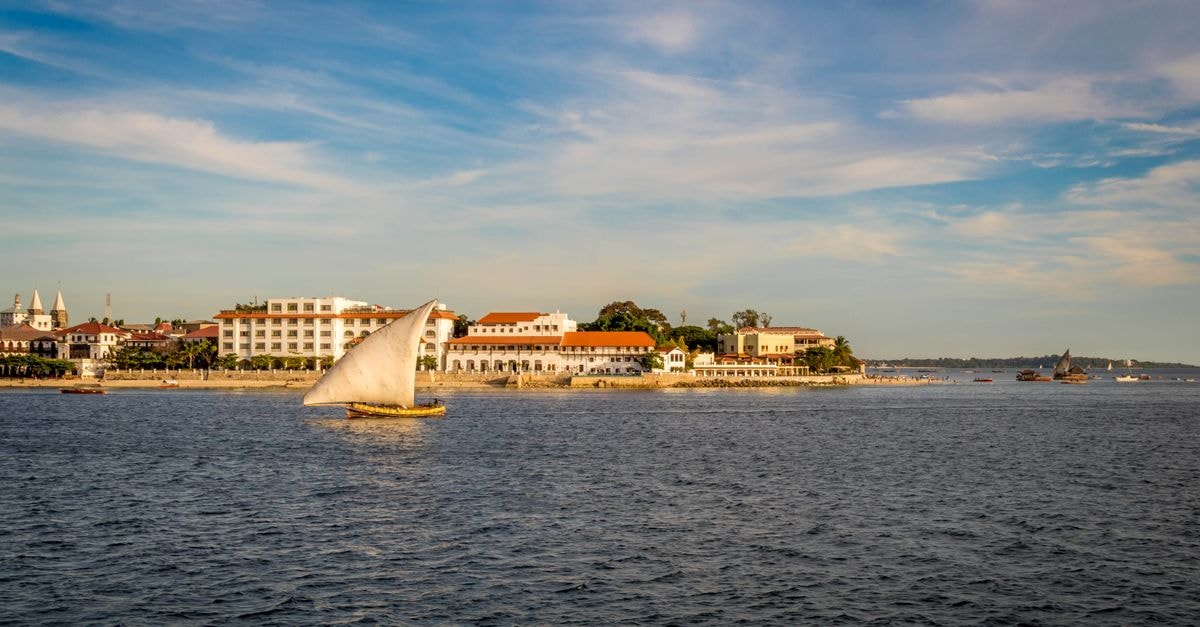 Charming sailboat on the vibrant waters of Zanzibar against a historic cityscape.