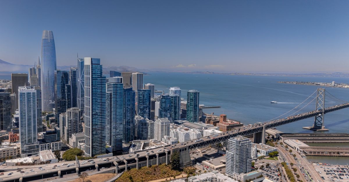 A stunning aerial view of San Francisco's iconic skyline and Bay Bridge over a clear blue sky.