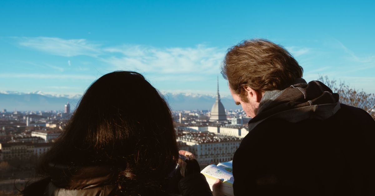 Traveling couple examines map with view of Turin and Mole Antonelliana in the background.