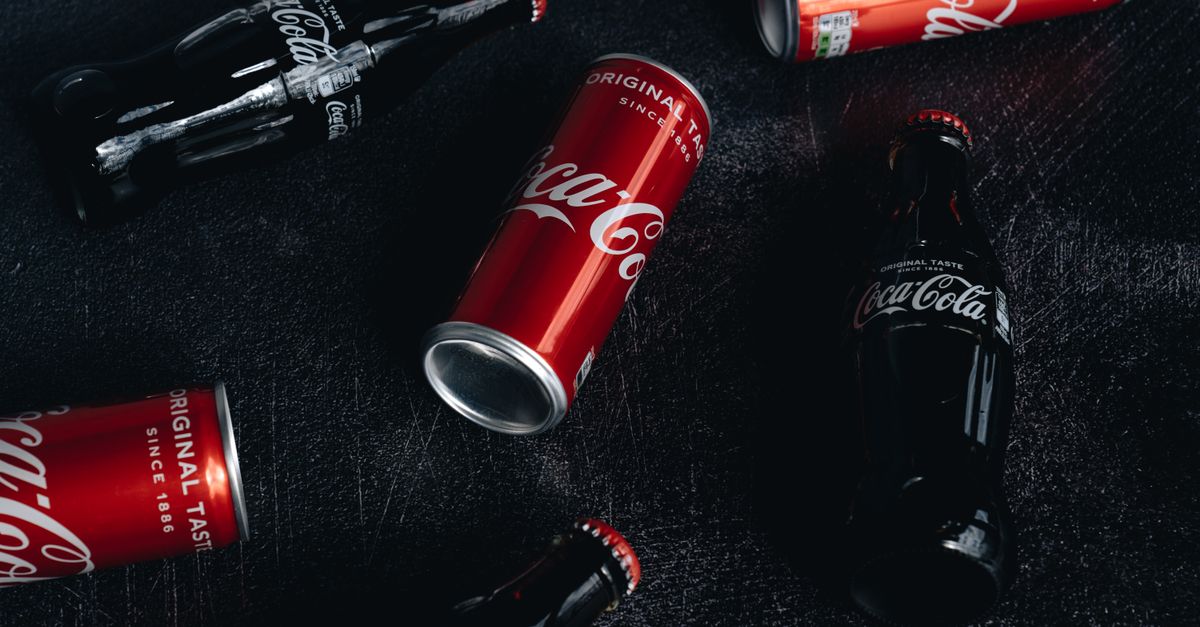 Coca-Cola deploys Adobe-built AI brand system across 200 markets as Fairlife unit hit by ransomware Coca-Cola cans and bottles artfully arranged on a textured dark surface.