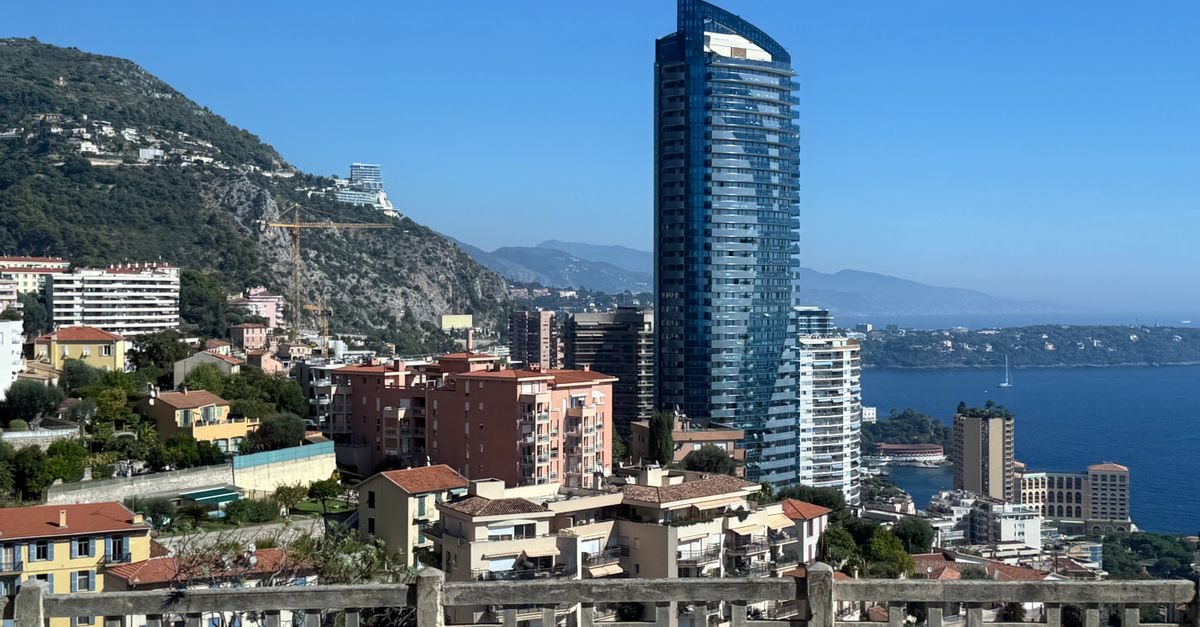 Monaco Travel Guide: Planning Tips, Costs and Things to Do Vibrant view of Monaco's coastline with modern skyscrapers and scenic mountains under a clear blue sky.