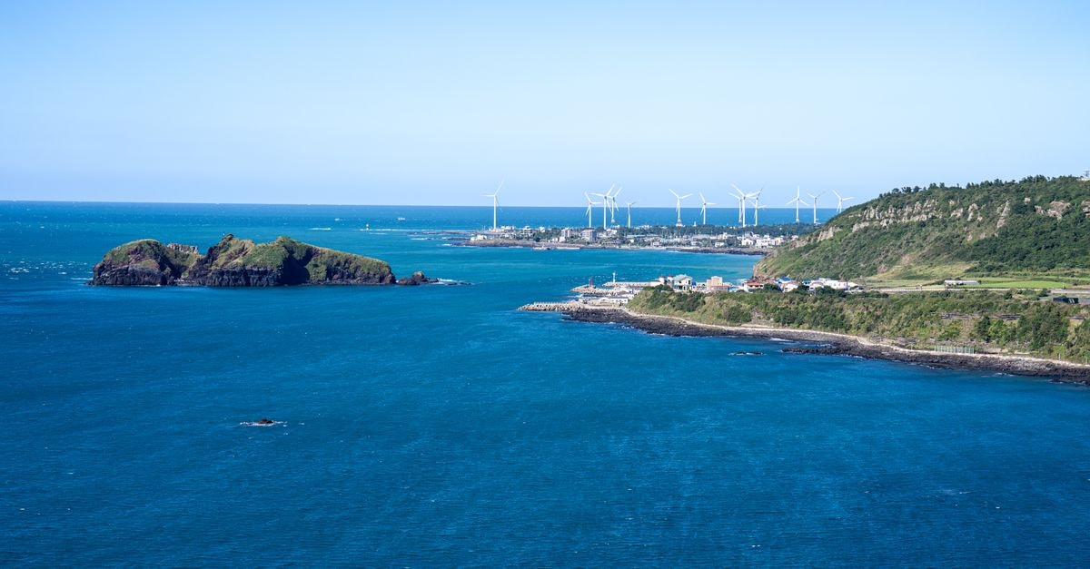 Cheonan Travel Guide for August: Planning Tips and Costs Scenic view of Jeju Island coastline with wind turbines under clear blue skies.