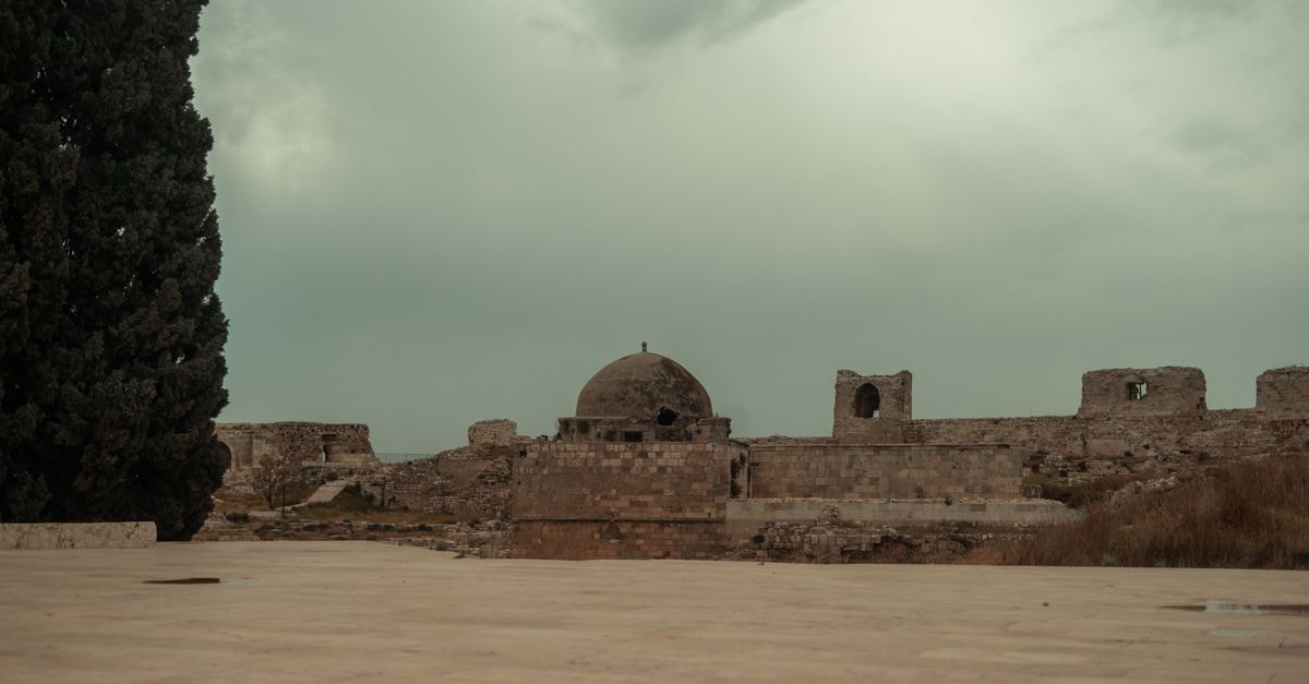 Riga Palace in Aleppo: A Quiet Retreat on Zaki el Arzouzi Street Rooftop view of an ancient citadel in Aleppo, Syria, featuring stone walls and a dome under a cloudy sky.