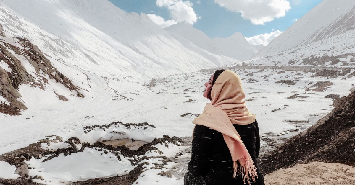 A woman sits on a snowy mountain, wrapped in a scarf, enjoying the serene winter view.