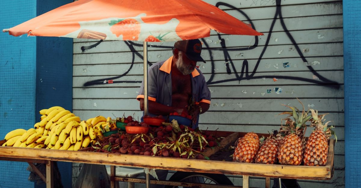 Chaguanas Travel Guide: Markets, Street Food and Local Rhythm A street vendor selling bananas and pineapples under a vibrant umbrella in an urban setting.