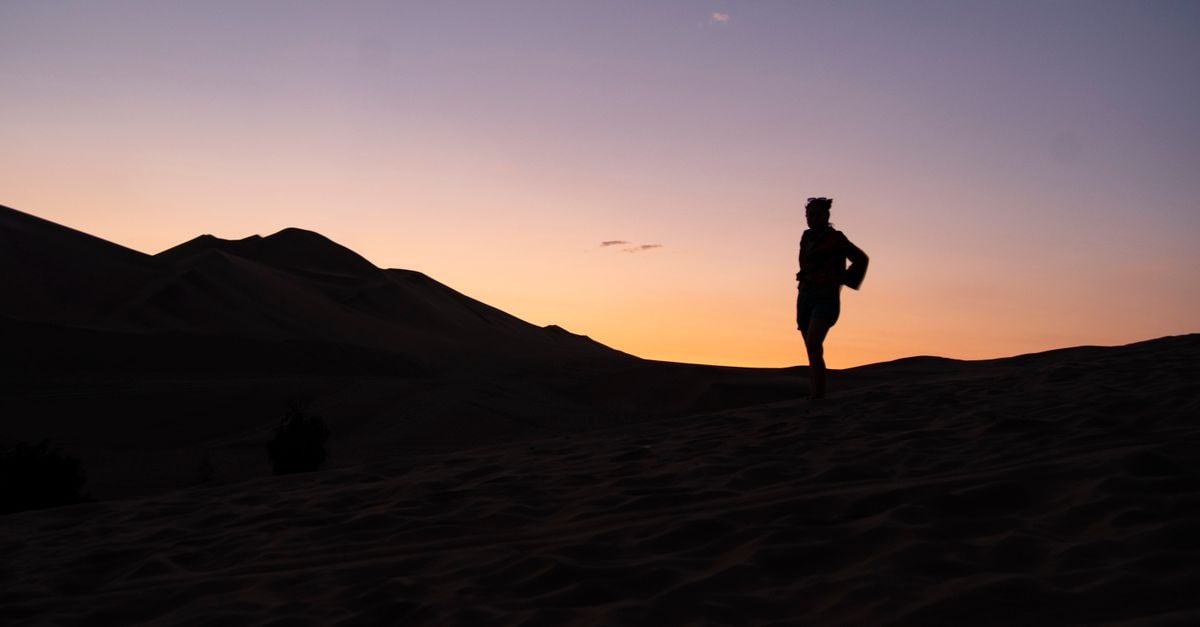 Person silhouetted against a dramatic sunset in the dunes of Ica, Peru, capturing a serene desert landscape.