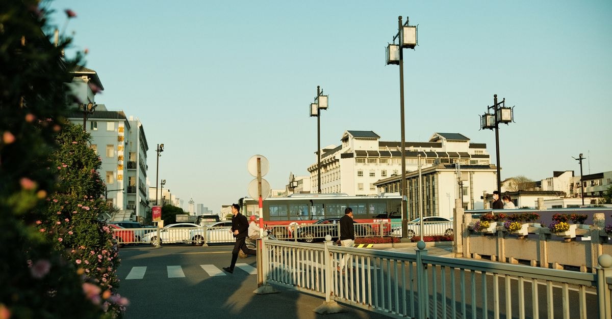 A city scene capturing pedestrians at a crosswalk with buildings and a red bus in the background.