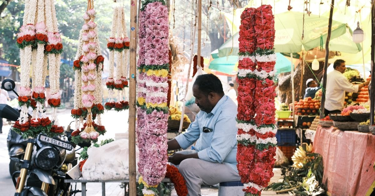 A colorful market stall in Bengaluru featuring vibrant flower garlands and a vendor.