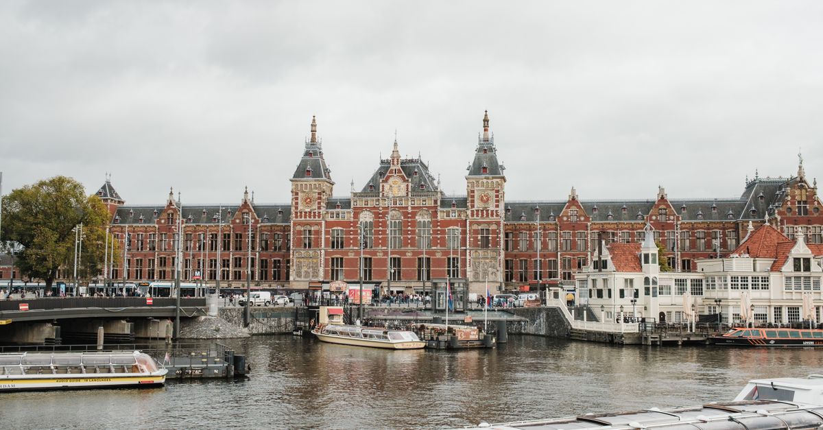 Iconic view of Amsterdam Centraal Station with boats on the river, showcasing urban architecture.