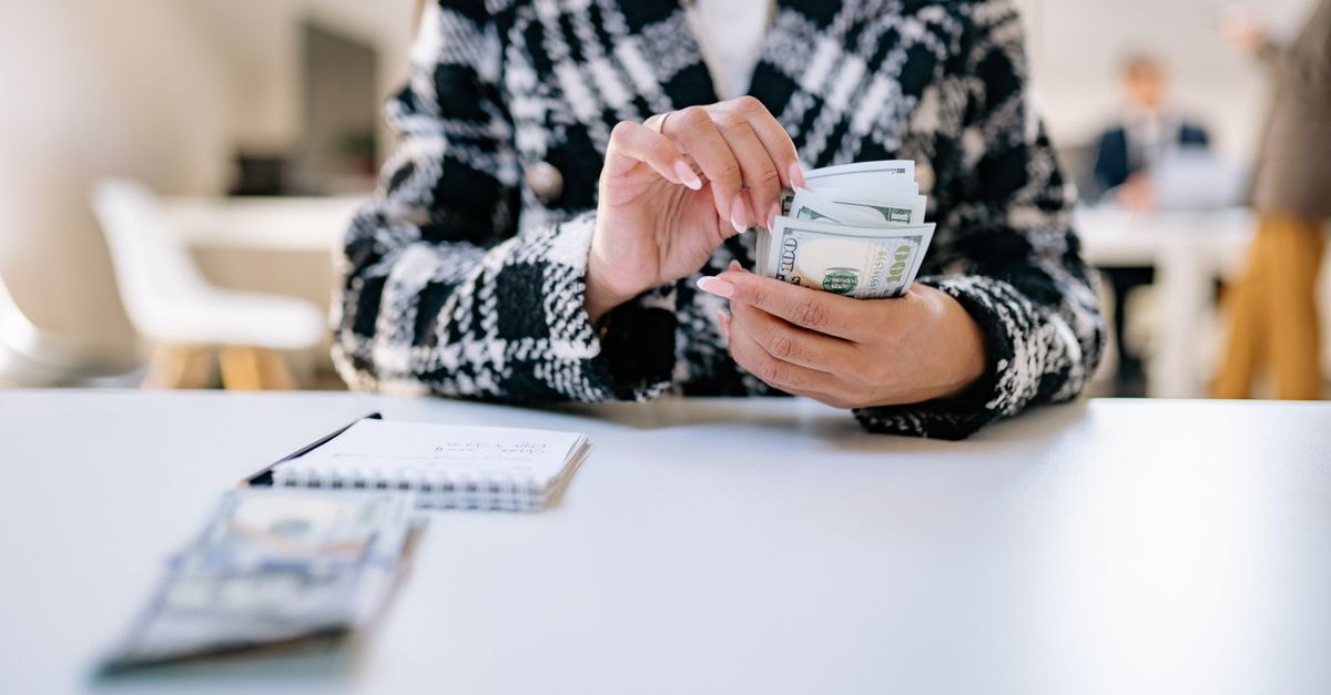 A close-up of a woman counting US dollars in an office environment, symbolizing financial management.