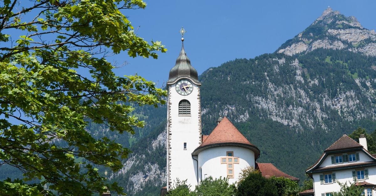 Scenic view of a quaint chapel nestled in the Swiss Alps surrounded by vibrant greenery and mountains.