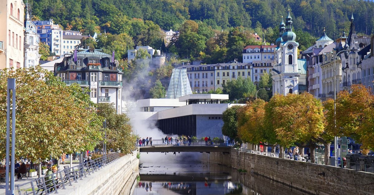 Scenic view of Karlovy Vary with colorful architecture, river, and autumn trees.