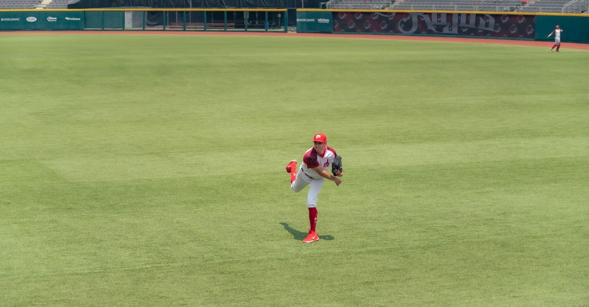 A baseball player pitching on a grass field in an empty stadium.